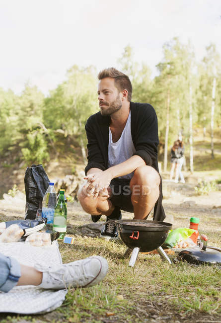 Man crouching by barbecue grill — Stock Photo
