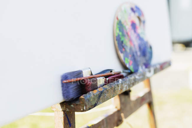 Paintbrushes and palette on easel — Stock Photo