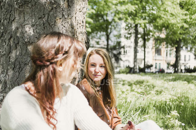 Amis féminins assis sur un terrain herbeux — Photo de stock