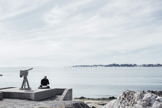 Человек, сидящий рядом с телескопом на море — стоковое фото