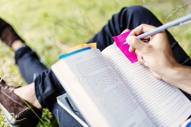 Student writing on adhesive note in book — Stock Photo