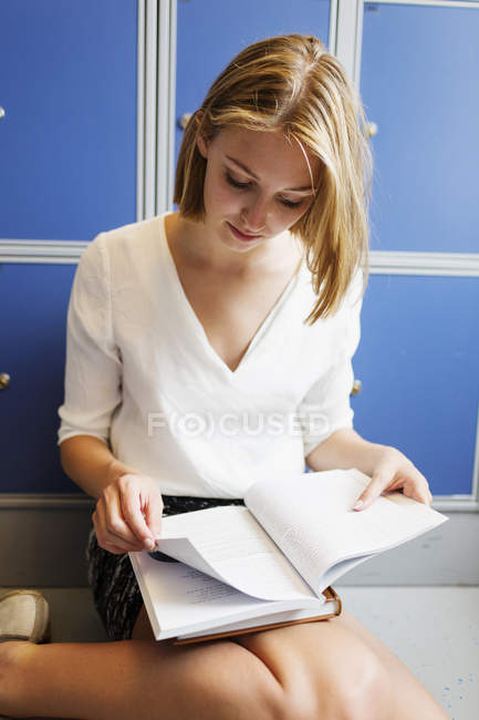 Mujer joven leyendo libro por casillero - foto de stock