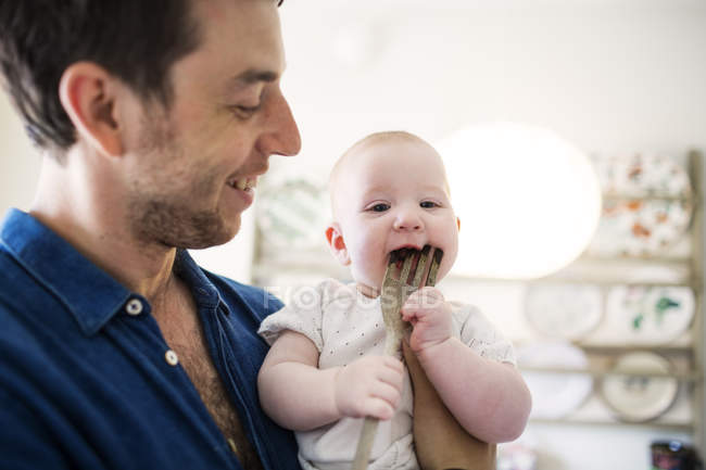 Pai olhando para bebê mordendo garfo — Fotografia de Stock