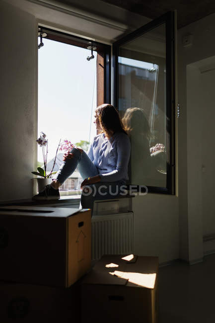 Jeune femme assise sur le rebord de la fenêtre — Photo de stock