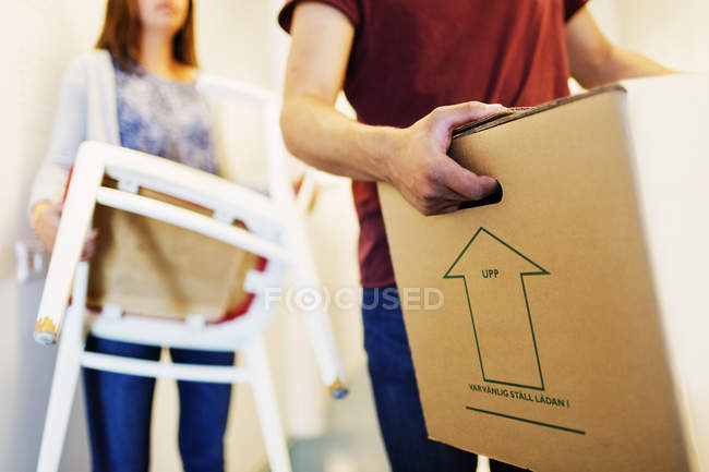Man holding box and woman carrying chair — Stock Photo