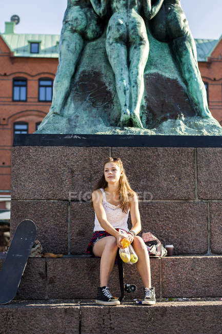 Girl sitting by statue — Stock Photo