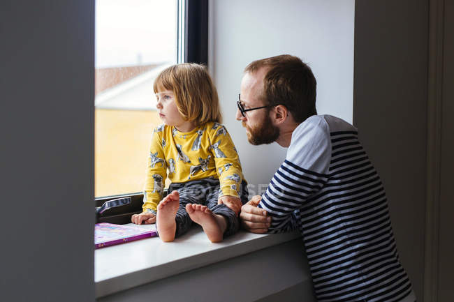Мужчина с дочерью смотрят в окно — стоковое фото