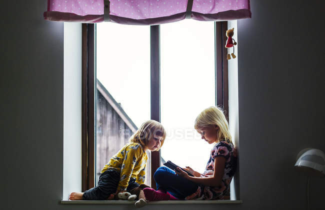 Девушка смотрит сестра с помощью цифрового планшета — стоковое фото