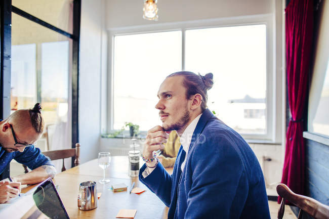 Вдумчивый молодой бизнесмен сидит за столом — стоковое фото