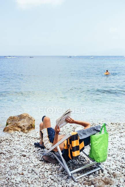 Человек, читающий газеты на берегу моря — стоковое фото