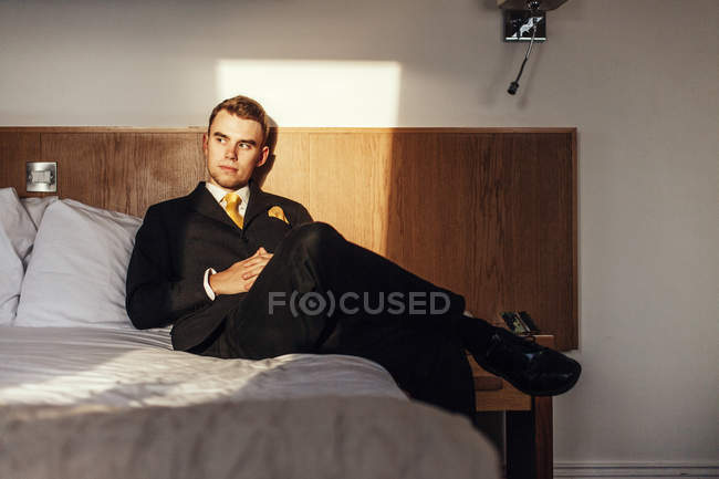 Hombre de negocios sentado en la cama en la habitación de hotel - foto de stock