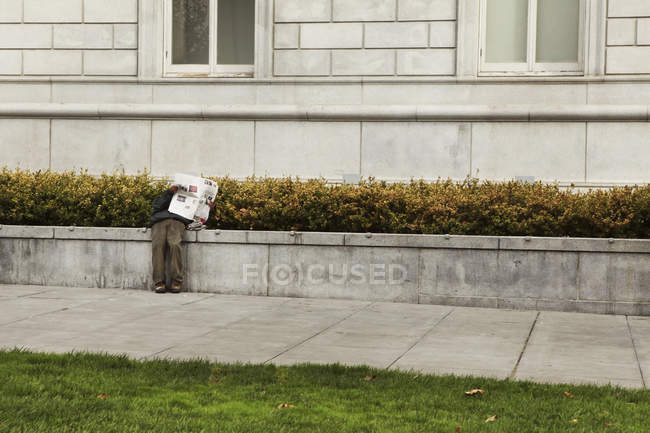 Hombre leyendo periódico por edificio - foto de stock