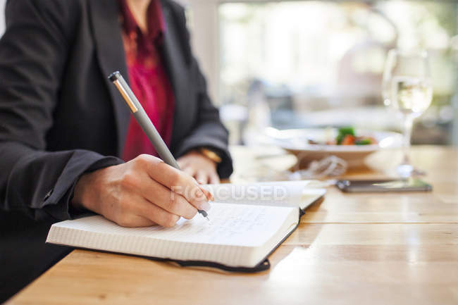 Midsection of businesswoman writing in book — Stock Photo