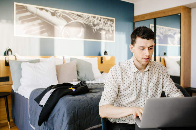 Homem usando laptop contra a cama — Fotografia de Stock