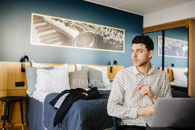 Человек с ноутбуком против кровати — стоковое фото