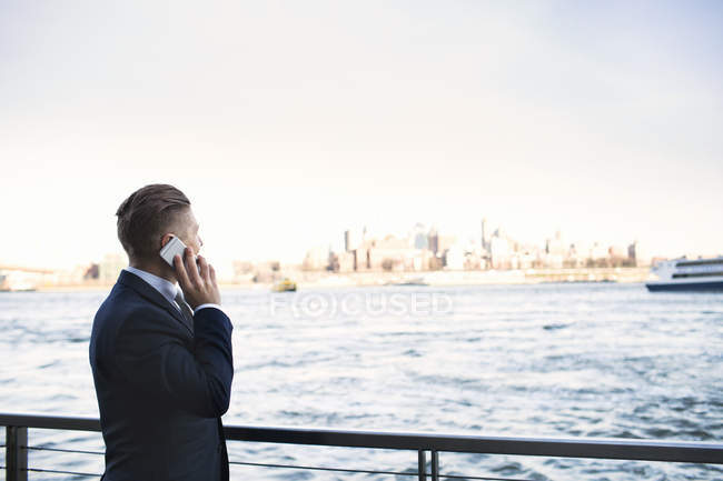 Businessman talking on smartphone while standing by river — Stock Photo