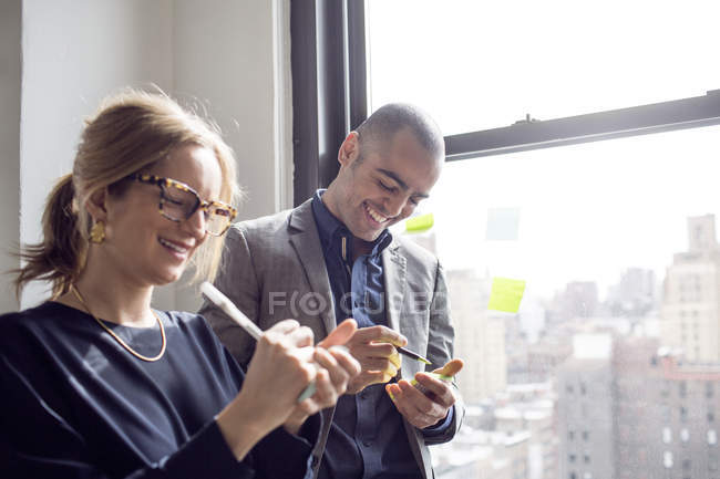 Businessman and businesswoman writing on sticky notes — Stock Photo