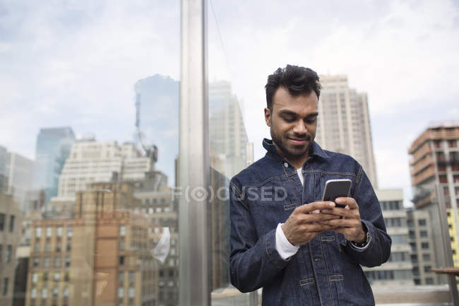 Man using phone while standing by window at rooftop — Stock Photo