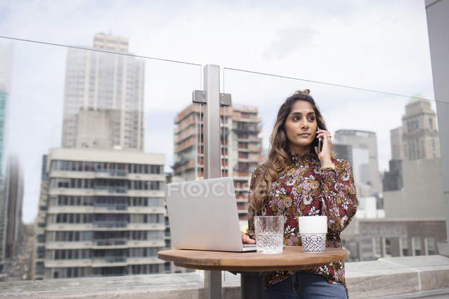 Woman using phone and laptop at rooftop restaurant — Stock Photo