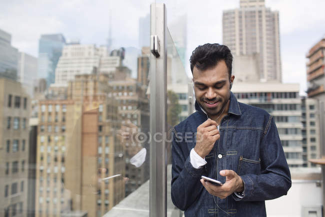 Hombre usando el teléfono mientras está parado junto a la ventana en la azotea - foto de stock