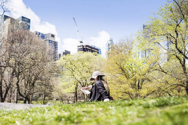 Femme assise sur l'herbe contre les arbres et les bâtiments — Photo de stock