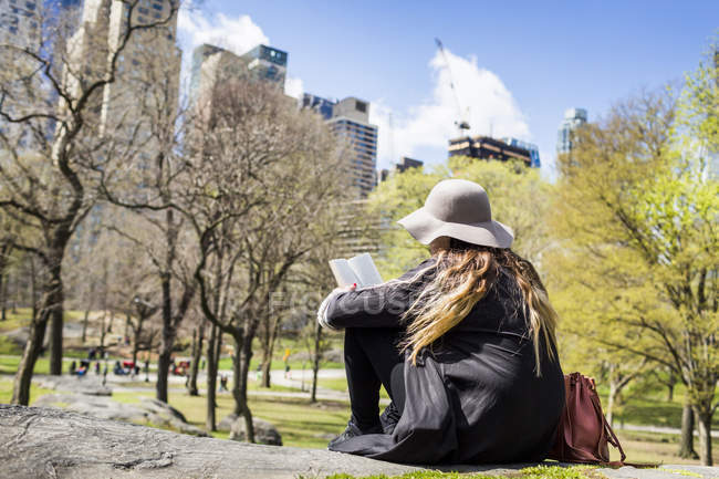 Mulher ler livro enquanto sentado no rock — Fotografia de Stock