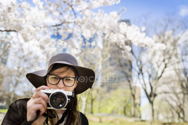Woman with camera standing against trees — Stock Photo