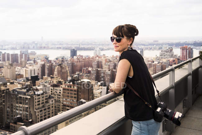 Жінка з камерою дивиться на міський пейзаж — стокове фото