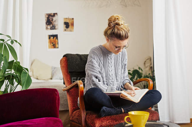 Woman writing on book while sitting on chair — Stock Photo