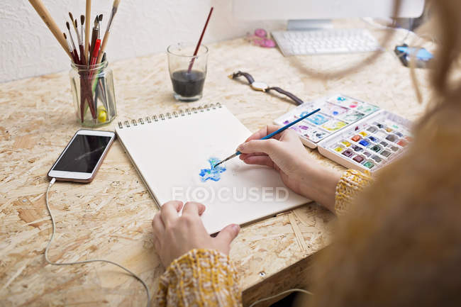Frau malt am Tisch auf Notizblock — Stockfoto