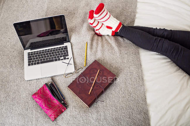 Femme se reposant par ordinateur portable et réserver sur le lit — Photo de stock