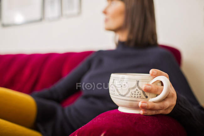 Femme tenant tasse de café sur canapé — Photo de stock