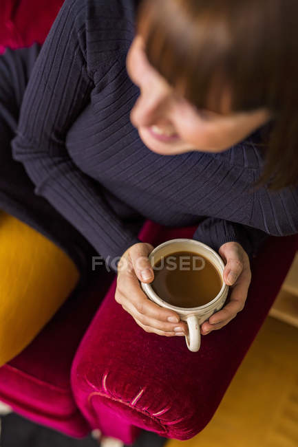 Mulher segurando xícara de café no sofá — Fotografia de Stock