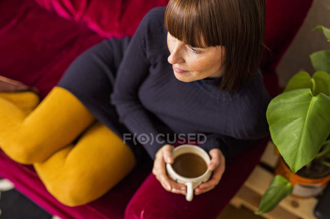 Frau hält Kaffeetasse auf Sofa — Stockfoto