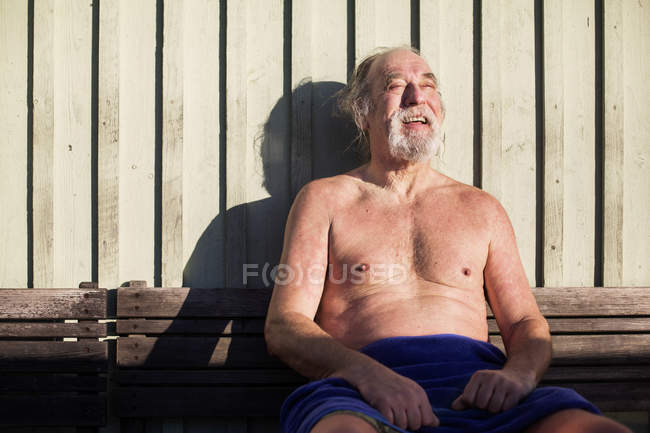 Человек расслабляется на скамейке против деревянной стены — стоковое фото