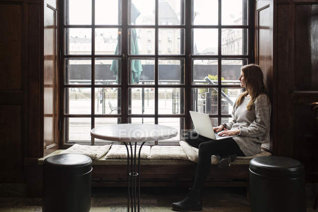 Женщина с помощью ноутбука, глядя в окно — стоковое фото