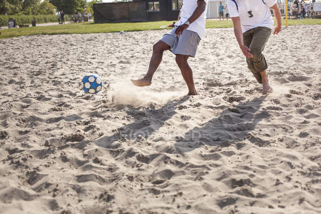 Друзья играют в футбол на пляже — стоковое фото