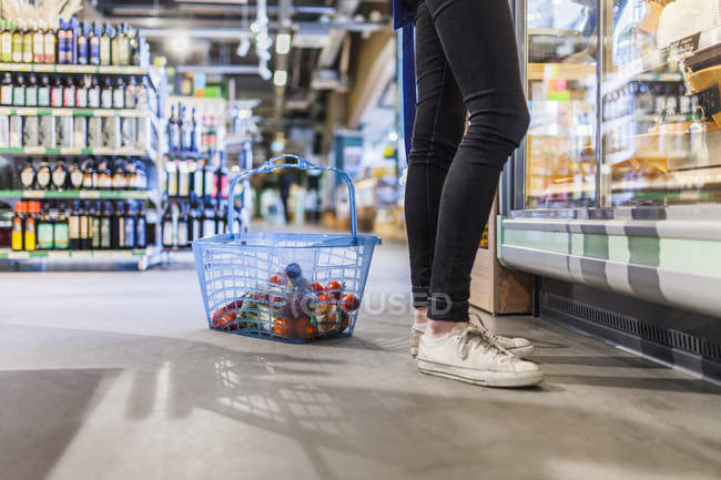 Jovem mulher em pé por cesta de compras — Fotografia de Stock