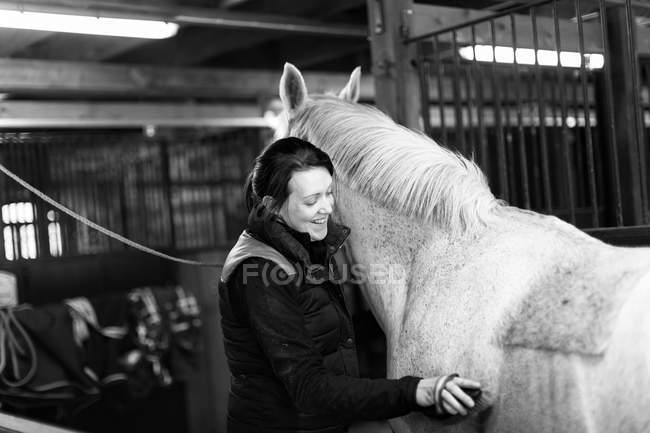 Donna spazzolatura cavallo in stalla — Foto stock