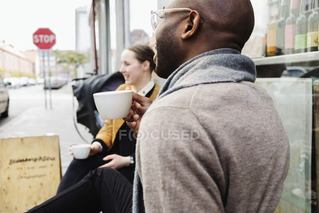 Freunde halten Tassen, während sie draußen sitzen — Stockfoto