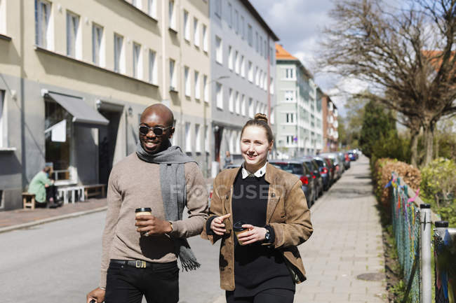 Amigos sosteniendo tazas de café mientras caminan en la ciudad - foto de stock