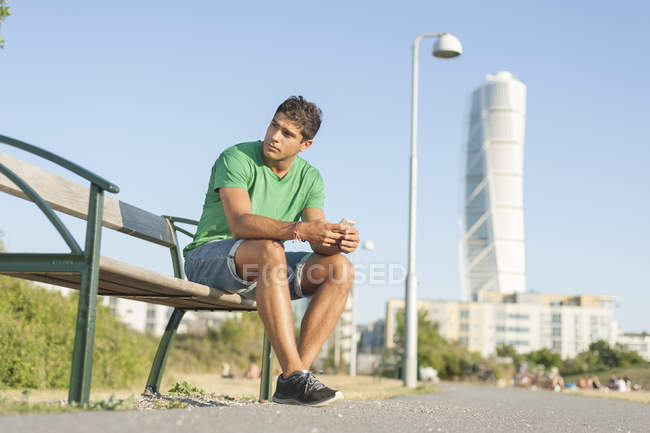 Joven sentado en el banco - foto de stock