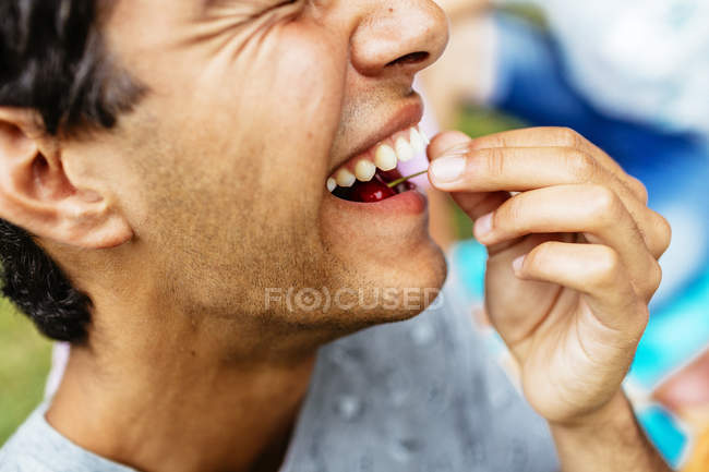 Cheerful young man eating cherry — Stock Photo