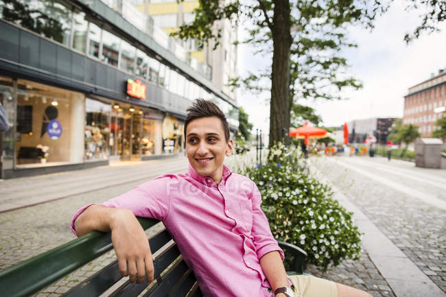 Lächelnder Mann sitzt auf Bank am Straßenrand — Stockfoto