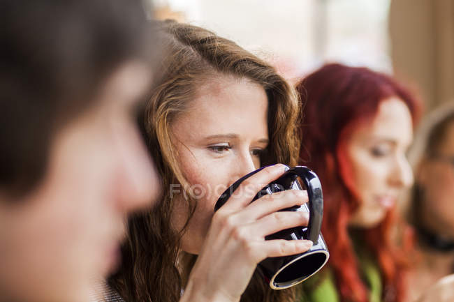 Woman drinking coffee amidst friends — Stock Photo
