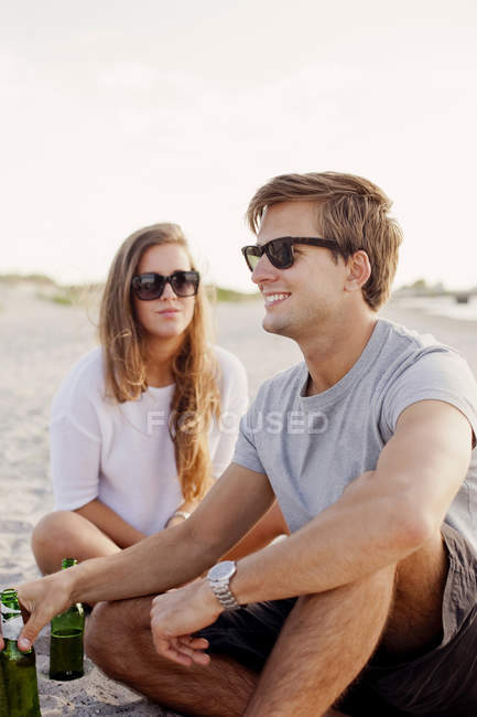 Homem sentado por amigo feminino na praia — Fotografia de Stock