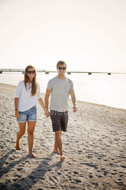 Couple holding hands while walking on shore — Stock Photo
