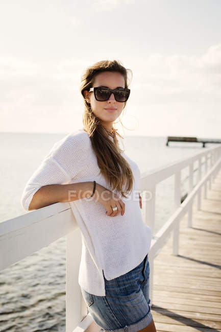 Mujer apoyada en barandilla de muelle sobre el mar - foto de stock