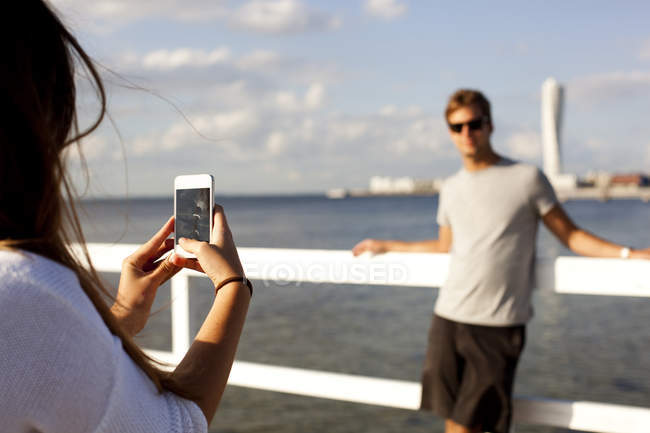 Woman photographing boyfriend by pier — Stock Photo