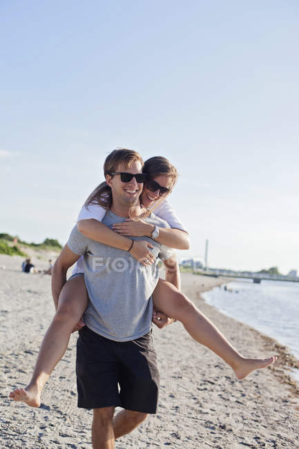 Couple enjoying piggyback ride at beach — Stock Photo